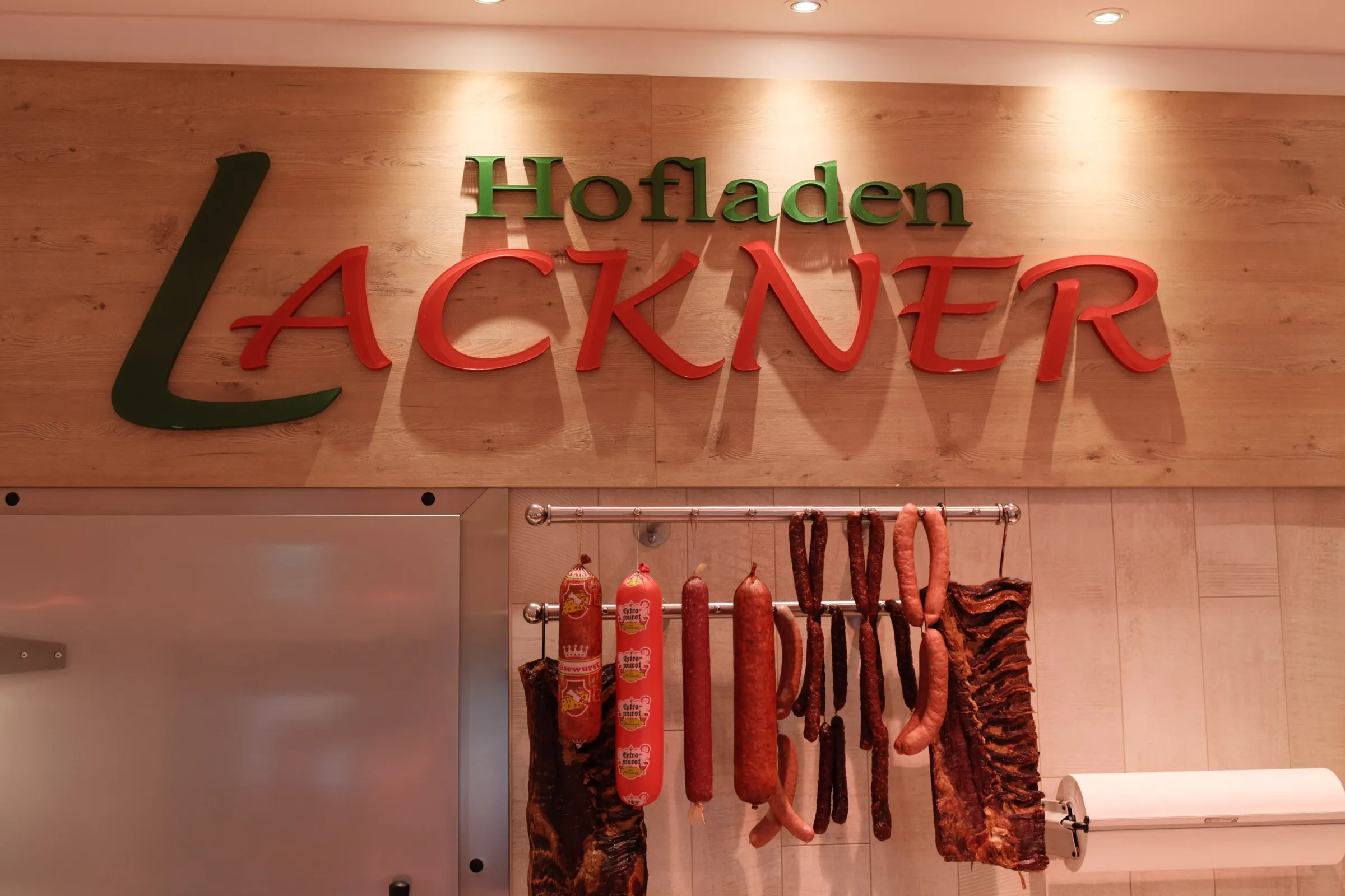 Logo des Hofladens Lackner mit Fleischspezialitäten im Hintergrund